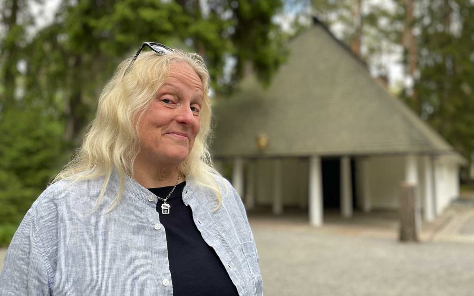 En kvinna framför ett kapell i en tallskog.